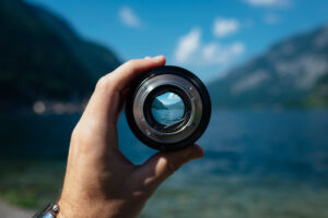 A hand holding a spy glass looking at mountains and a lake